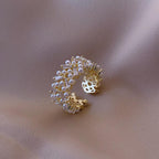 A gold-colored ring with simulated pearls set in a pave pattern, encircled by zircon accents on a textured background.