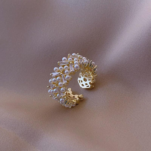 A gold-colored ring with simulated pearls set in a pave pattern, encircled by zircon accents on a textured background.