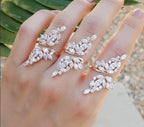 A person's hand wearing a multiple-band adjustable ring with wing-shaped designs, featuring round-cut cubic zirconia stones.