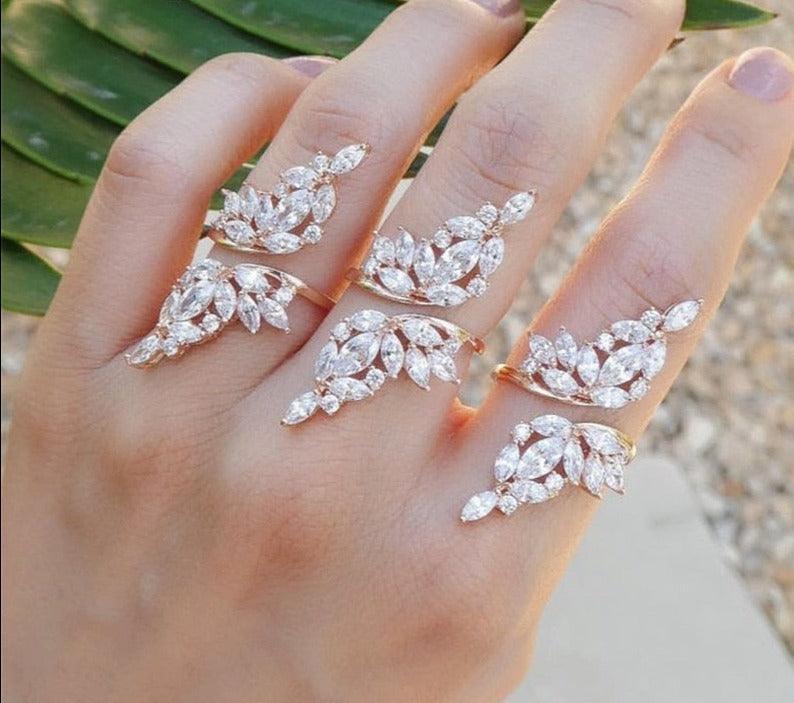 A person's hand wearing a multiple-band adjustable ring with wing-shaped designs, featuring round-cut cubic zirconia stones.