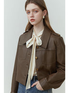 A woman wearing a brown PU leather jacket with a turn-down collar and a single-breasted closure, paired with blue jeans.